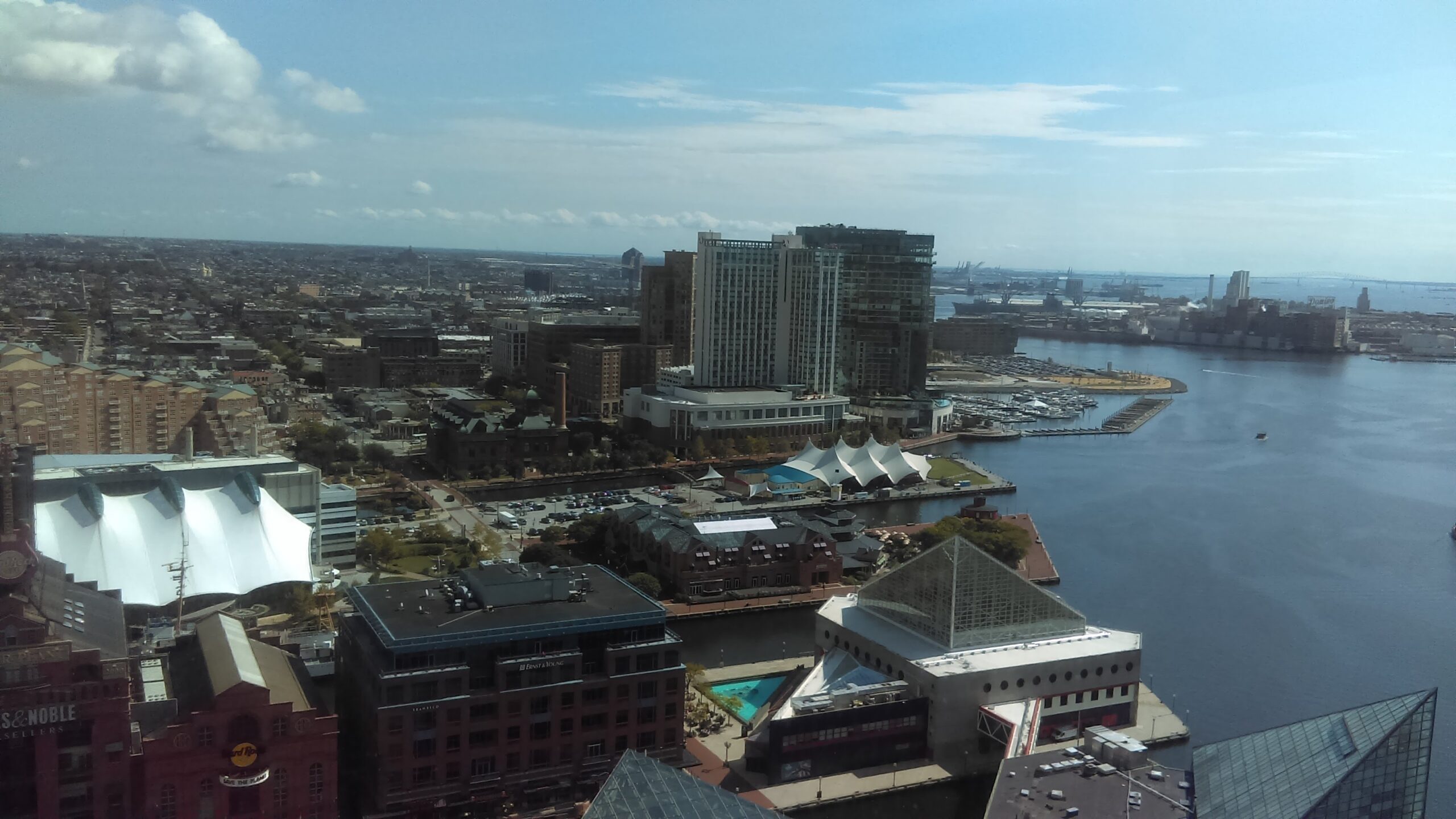 Aerial view of a waterfront cityscape showcasing modern buildings, marinas, and a tent structure, indicating a vibrant urban environment.