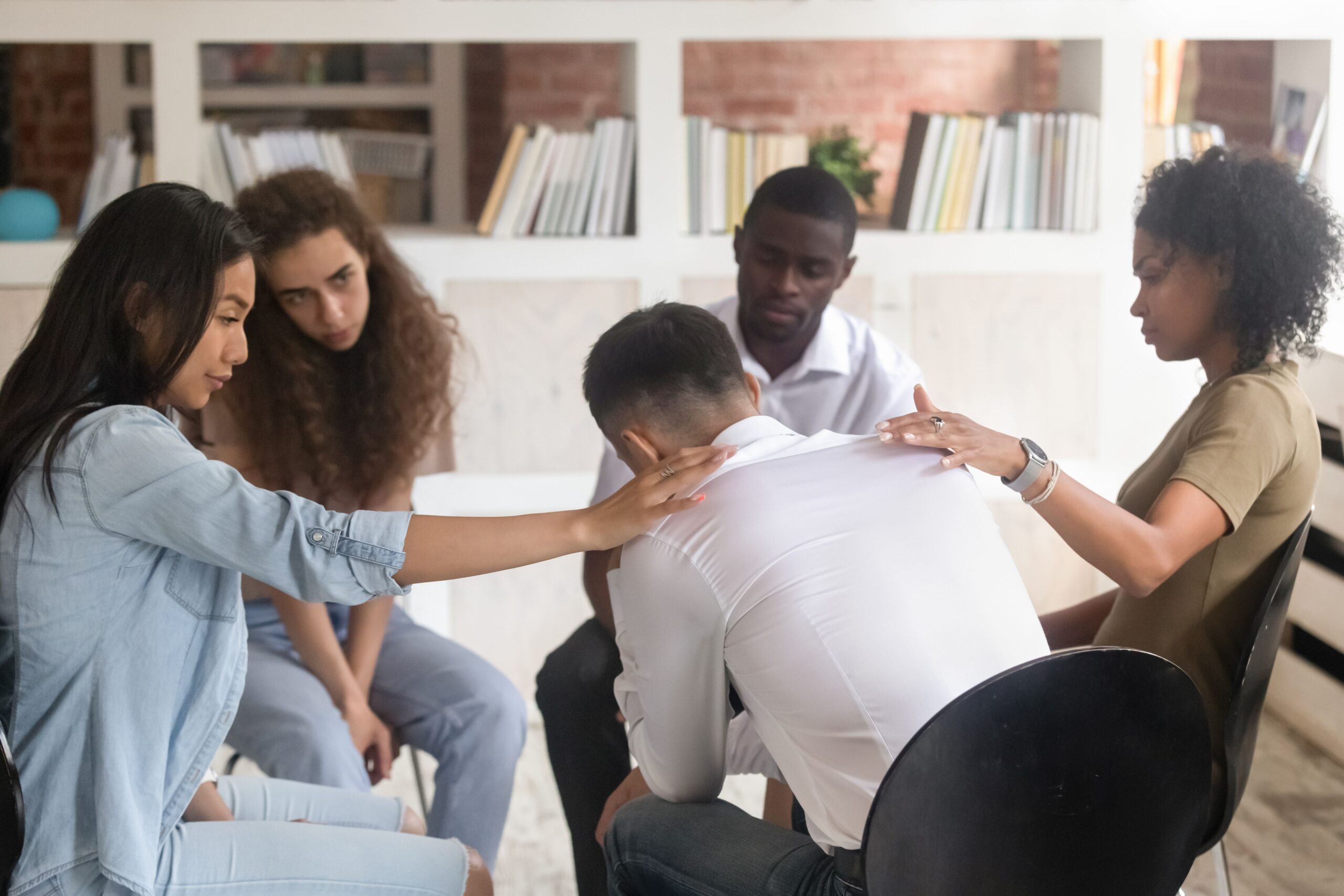 A supportive group surrounds a distressed person, offering comfort and empathy in a heartwarming scene. The setting suggests a moment of connection and healing.