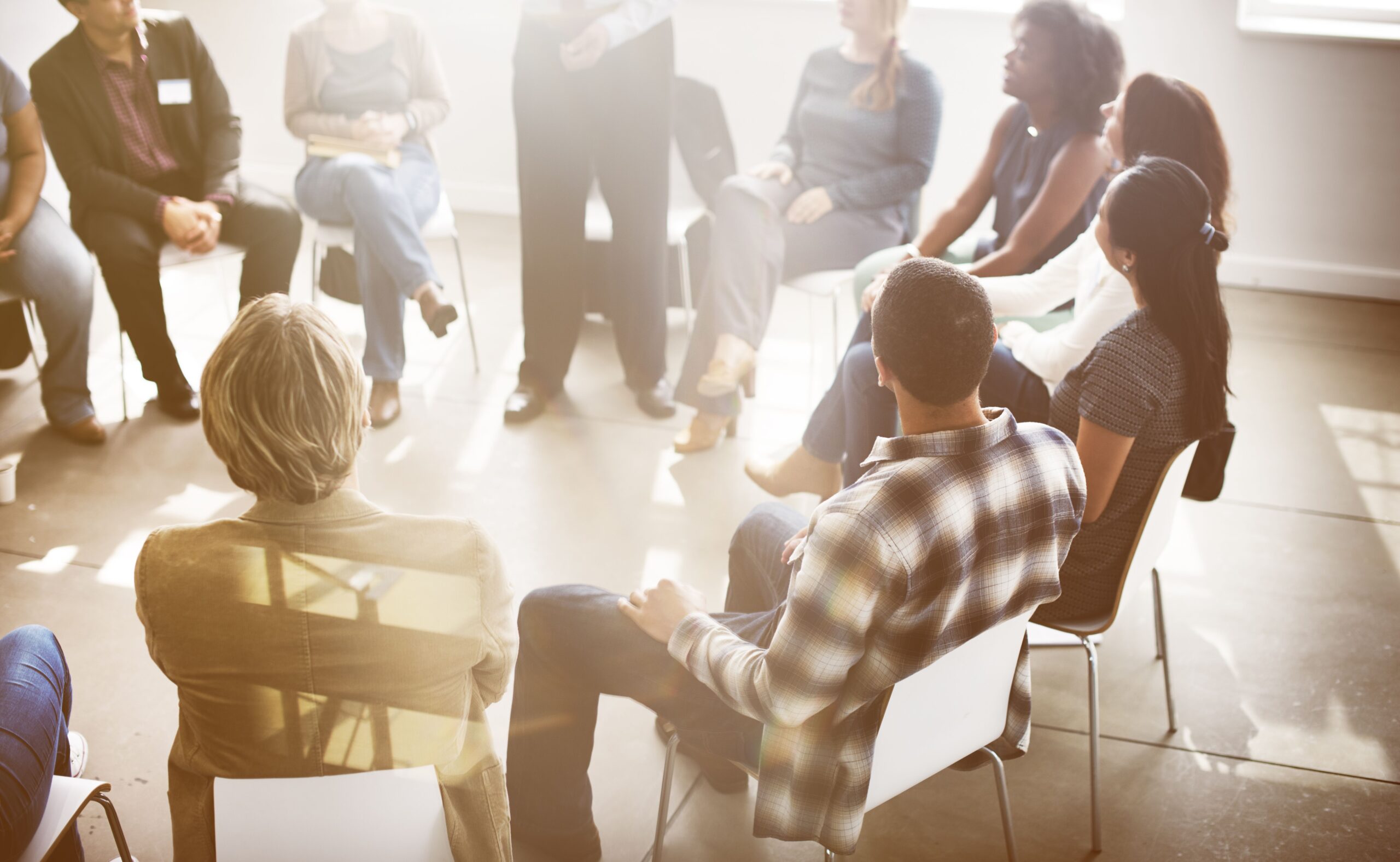 A diverse group of people seated in a circle, actively engaging during a discussion or meeting in a well-lit room.