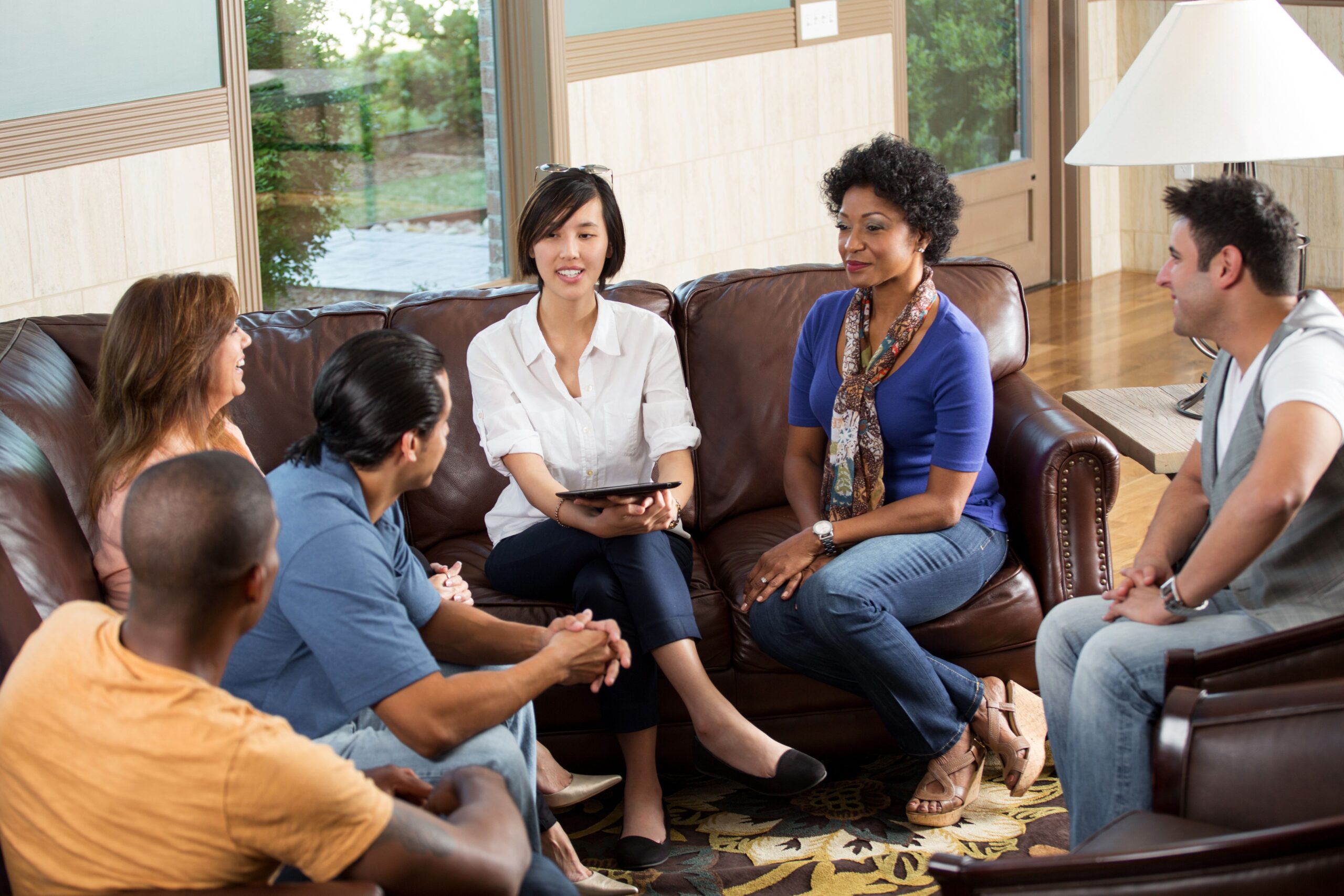 A diverse group of five people engages in a discussion while seated in a cozy living room, fostering collaboration and connection.