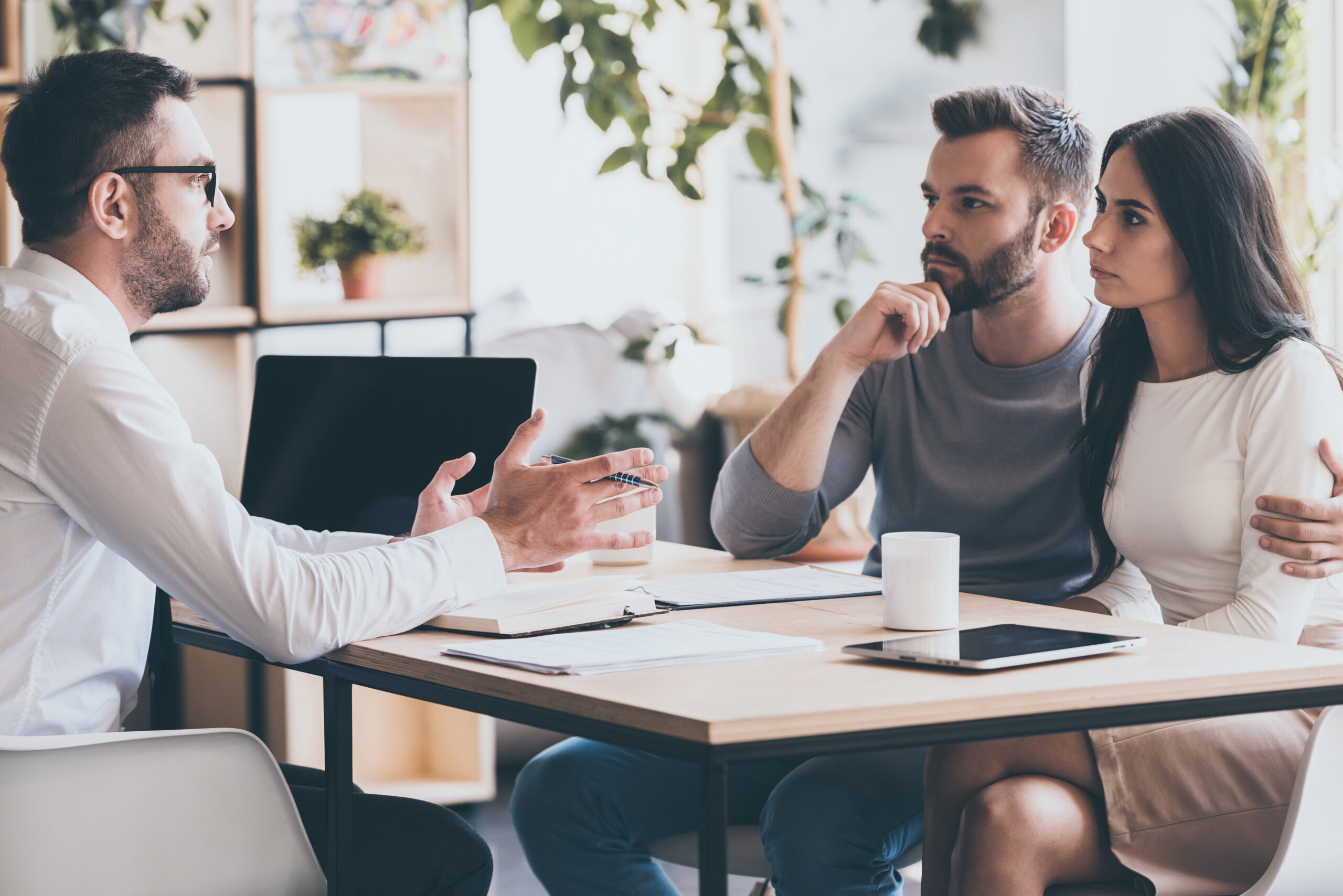 A financial advisor discusses options with a couple, who appear engaged and contemplative, in a modern office setting.